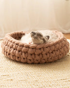 Handcrafted Solace Aura Merino wool cat bed in cappuccino brown, chunky knit design with cat resting inside on natural rug.