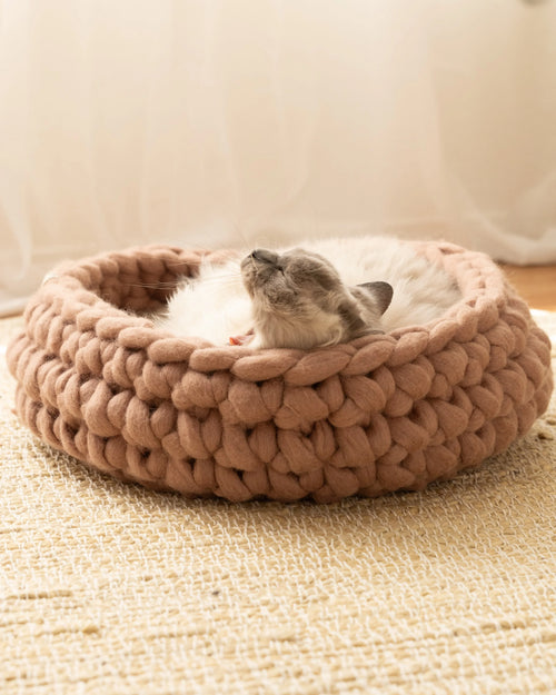 Handcrafted Solace Aura Merino wool cat bed in cappuccino brown, chunky knit design with cat resting inside on natural rug.