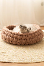 Handcrafted Solace Aura Merino wool cat bed in cappuccino brown, chunky knit design with cat resting inside on natural rug.